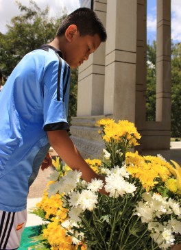 A young man pays respect to the victims of the Killing Fields & lays a bouquet of flowers outside the site's memorial. 