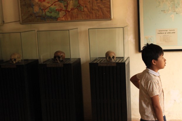 A child visitor walks past exhibit cases with skulls on display at Tuol Sleng. 